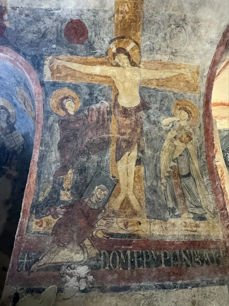 Uno degli affreschi celebri della cripta: la Crocifissione con l’Abate Epifanio inginocchiato ai piedi della croce, raffigurato con il nimbo quadrato riservato ai viventi.